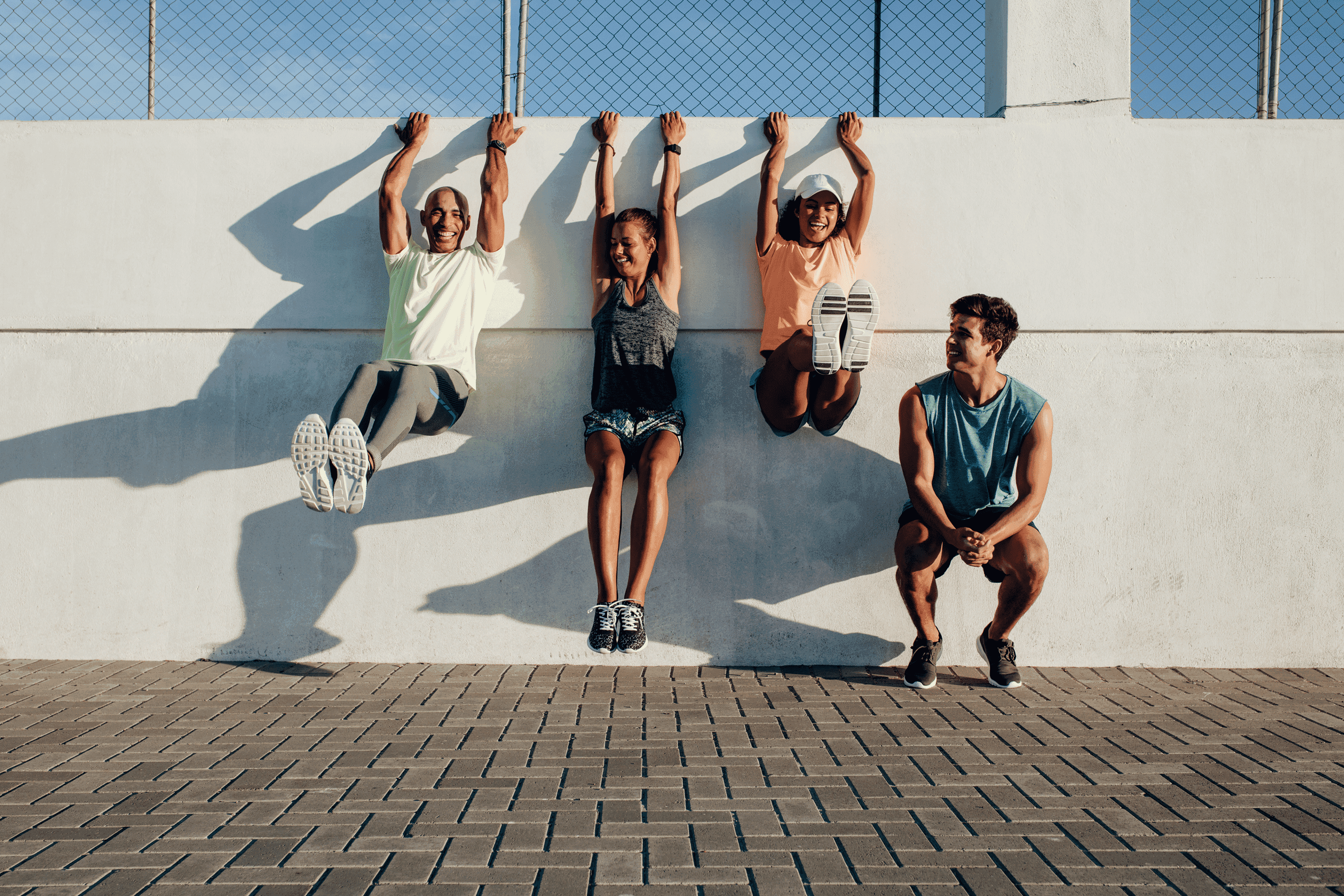 Friends laughing as they hang from a sunny wall